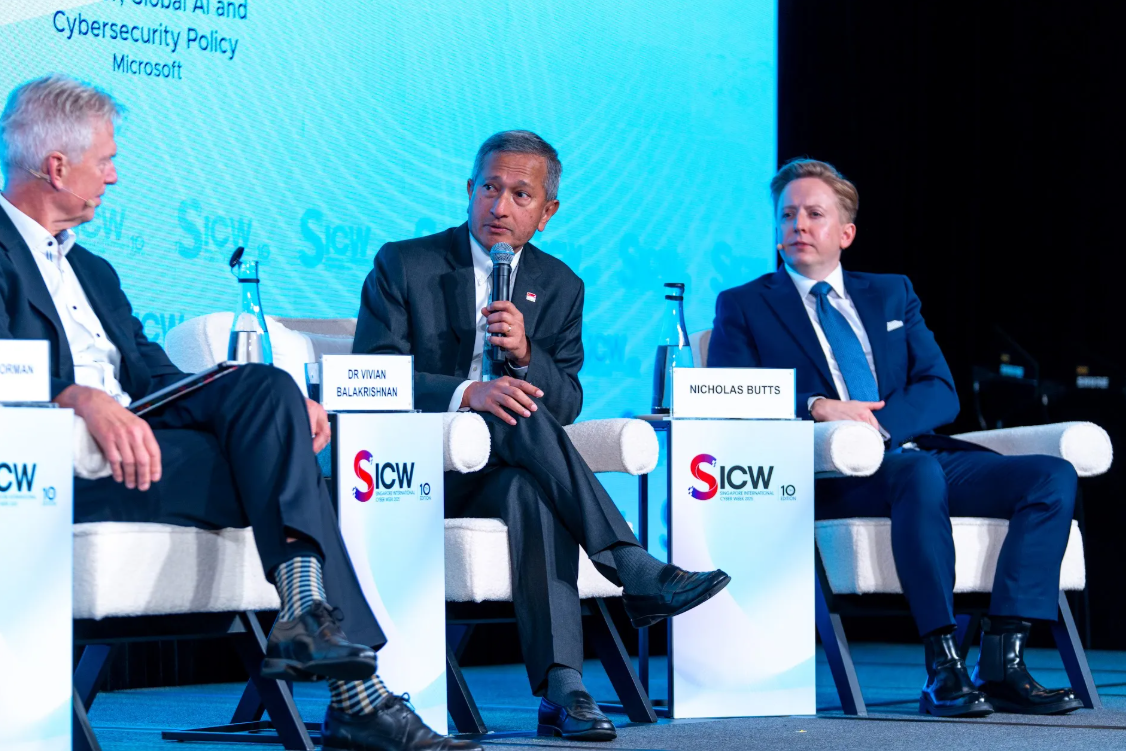 Three men on a stage at "SICW 10" speak at a panel discussion.